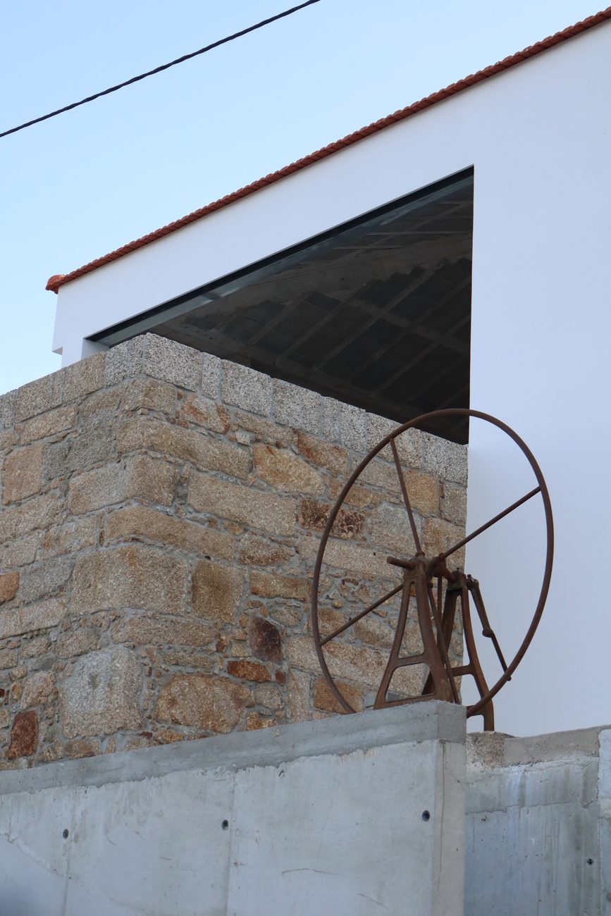 Muro de granito com roda em ferro e cobertura branca — Edifício de restauração Leitão do Petti, Penafiel
